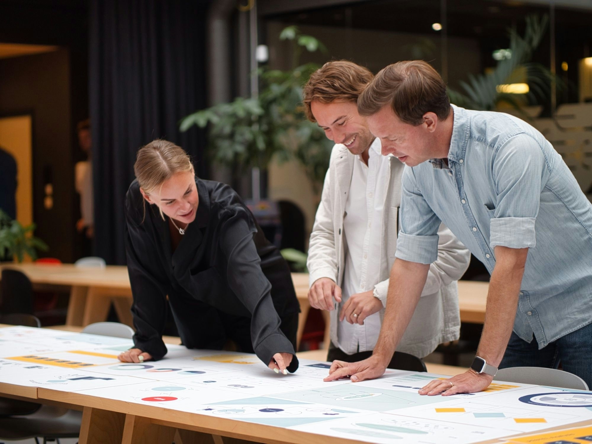 Three designers leaning over an insight map and discussing what they are looking at. Photo.